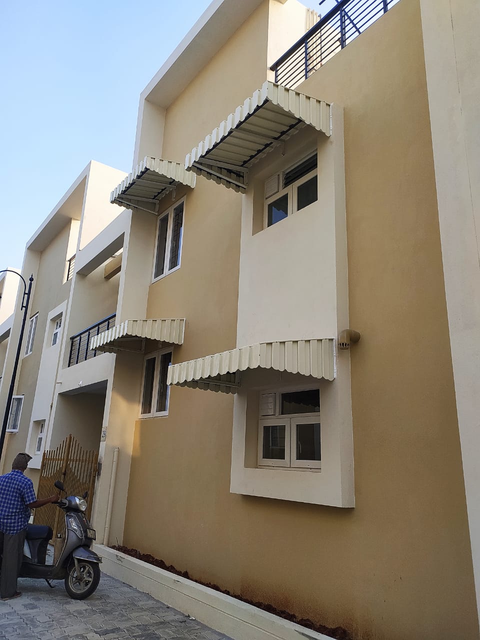 White aluminium window awnings installed on a modern residential building by Arasuvel Roofings in Tamil Nadu.