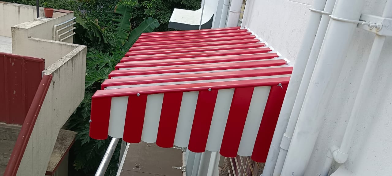 Red and white fixed aluminium window awning installed on a residential building by Arasuvel Roofings for sun and rain protection